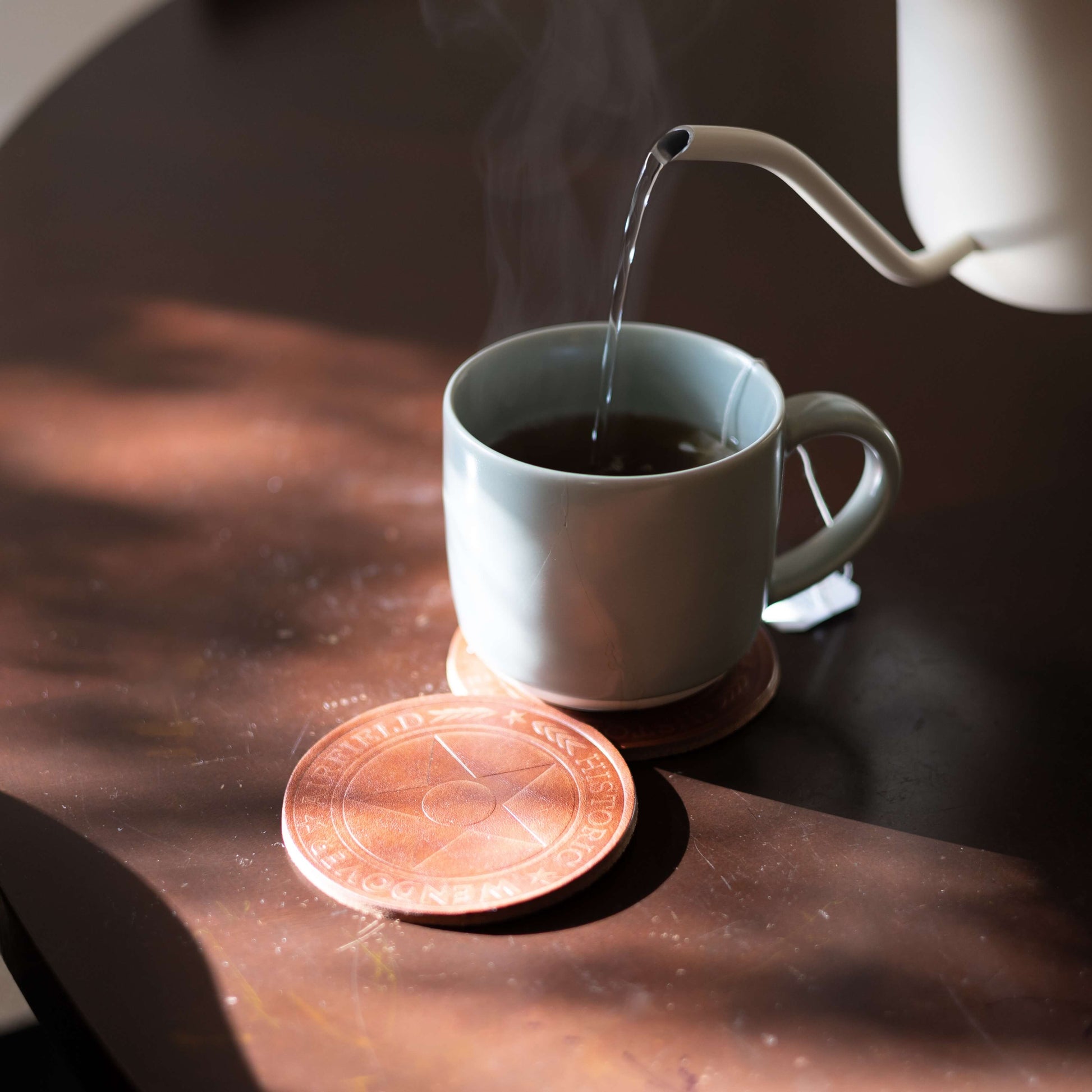 Tea being poured into a white mug on a wooden table with a custom logo coaster from Hutch & Hale.