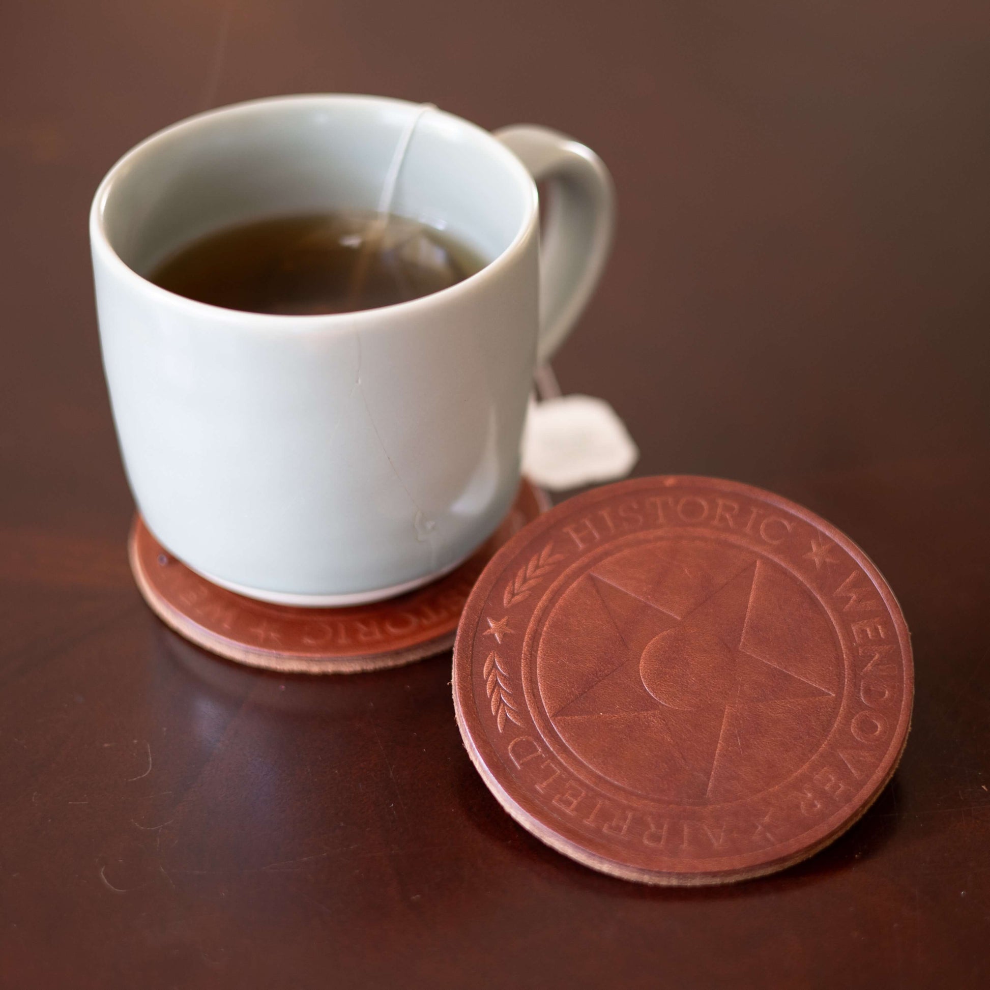White mug with tea on a brown surface with a custom logo coaster featuring a star design.