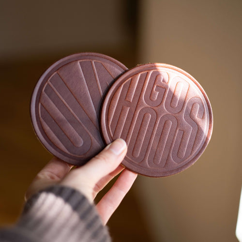 Custom logo coasters held by a hand against a blurred background.