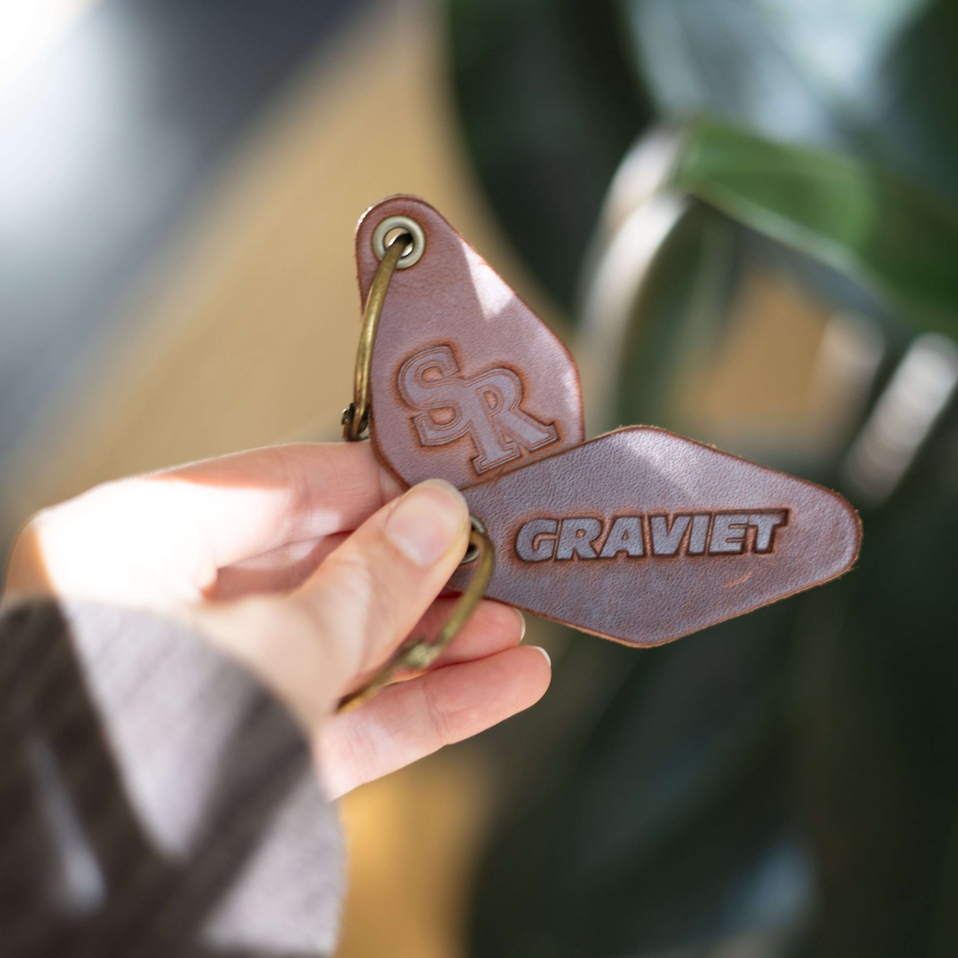 Hand holding a custom logo keychain that says "Graviet" with a blurred background