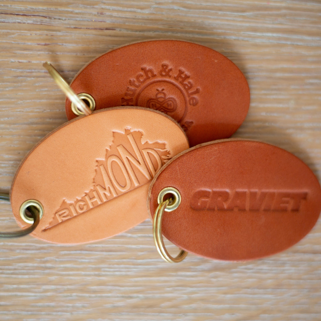 Three leather keychains with custom logos on a wooden surface