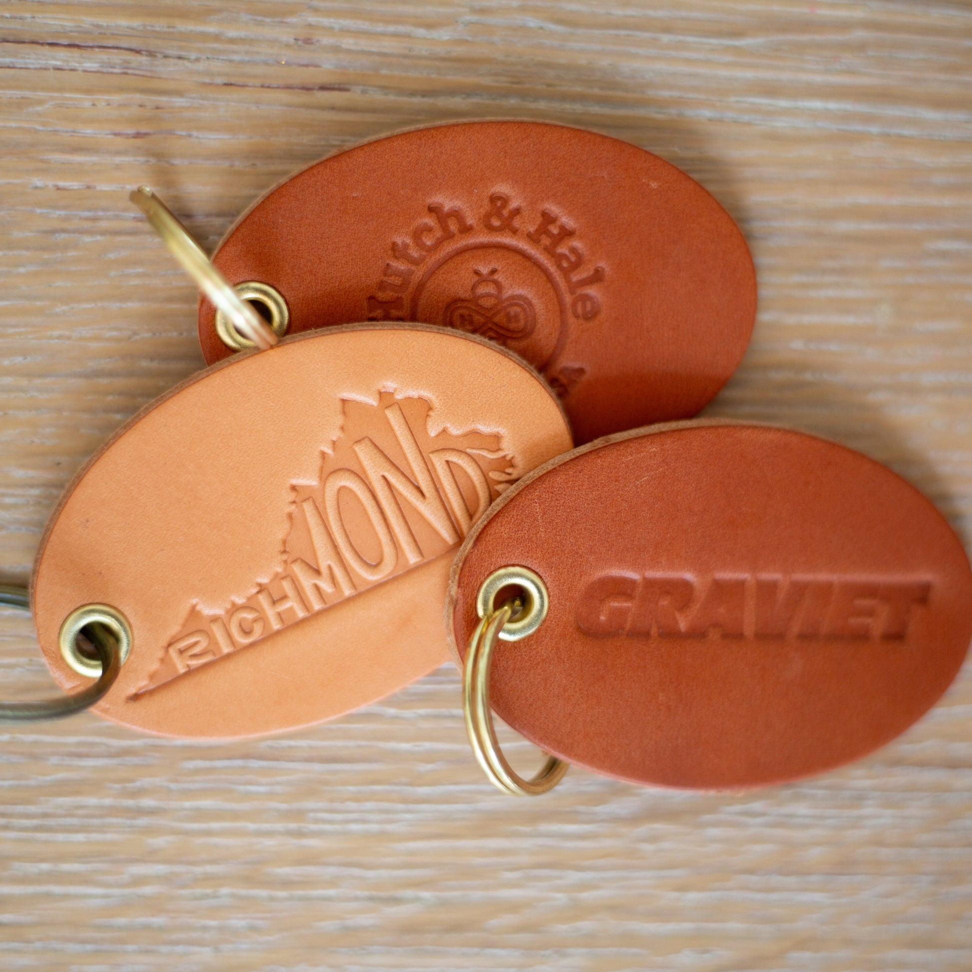 Three leather keychains with custom logos on a wooden surface
