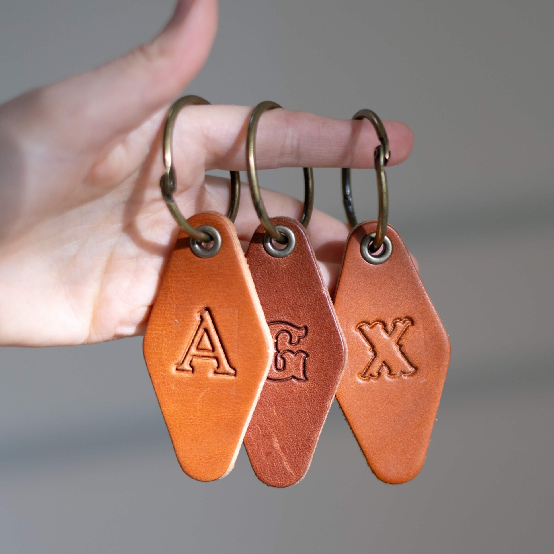 Hand holding three custom leather keychains with engraved letters against a neutral background